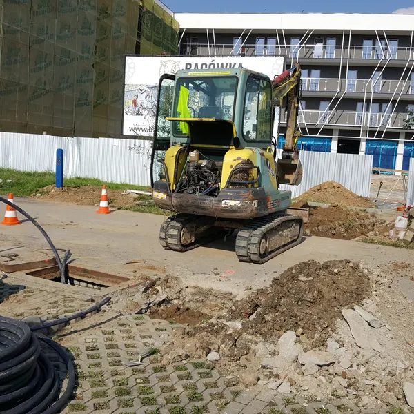 Minikoparka i zwoje czarnej mikrokanalizacji przy otwartej studni kablowej — budowa podziemnej trasy swiatlowodowej CityNet wzdluz ulicy w Rzeszowie.